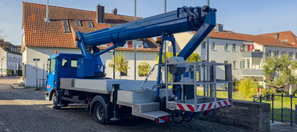 Blue truck-mounted aerial work platform with an extendable boom and man basket parked on a paved street